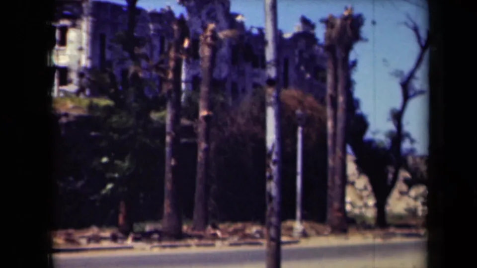 A 1944 Manila street view shows poles, trees, damaged-looking walls, and a partial building facade in soft color 8mm footage.
