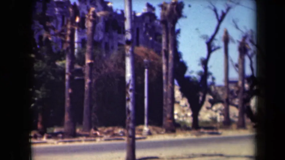 The Manila street scene continues with poles, bare trees, a damaged-looking wall, and a quiet roadway captured on faded 8mm film.