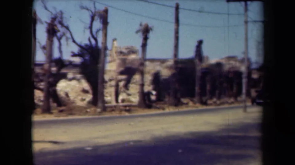1944 Manila roadside view with ruined structures, scorched palm trunks, overhead wires, and debris along the street.