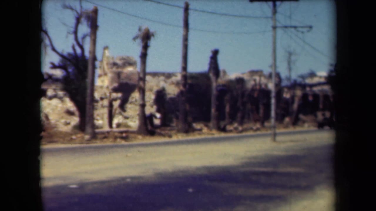 1944 Manila street view showing damaged buildings, scorched trees, utility lines, and debris beside an open roadway.