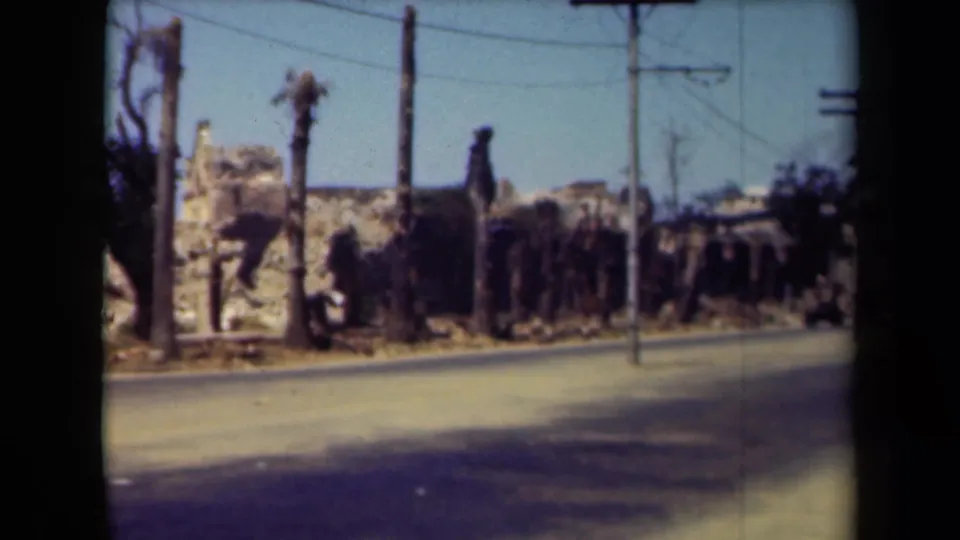 1944 Manila roadway with rubble, scorched palm trunks, damaged structures, utility poles, and a distant figure-like silhouette.
