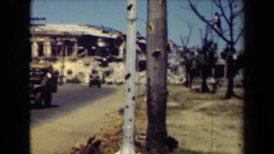 1940s Manila street view with a damaged building, roadside poles, sparse trees, and a military vehicle entering the frame.