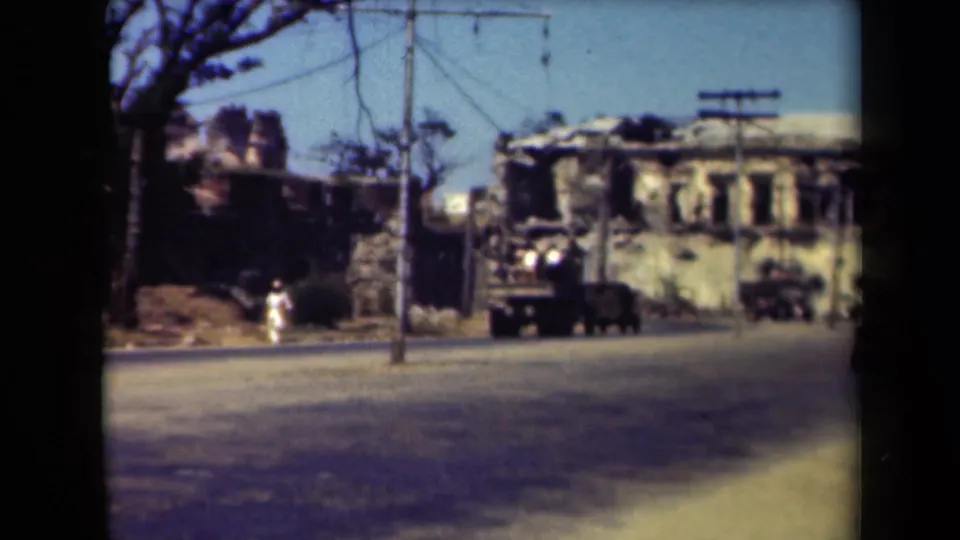 Manila wartime street view with military vehicles near a damaged building, utility pole, tree branches, and scattered debris.
