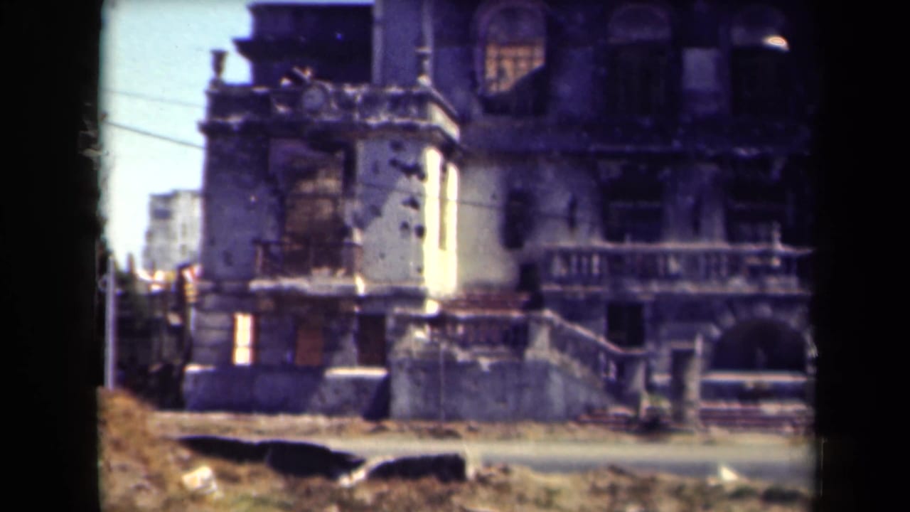 Damaged multi-story building with broken windows and dark film border.