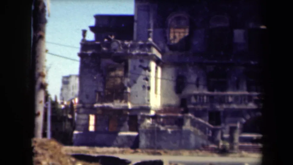 1944 Manila frame of a damaged multi-story facade with bullet-like marks, broken openings, balcony railings, and a street foreground.