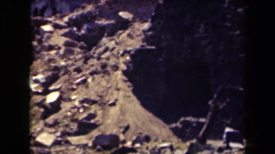 1944 Manila frame shifts to rubble and loose debris near the damaged structure, with soft focus and heavy shadow.