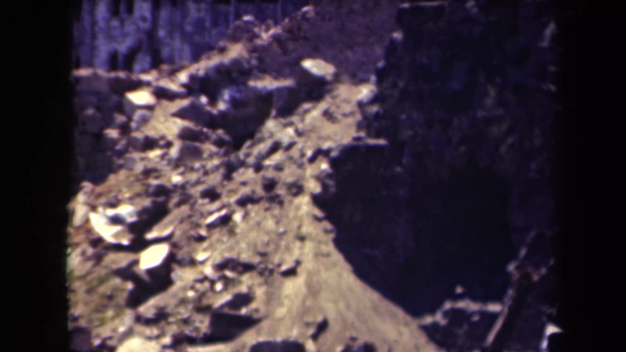 Rubble and a damaged building facade seen through dark film-frame edges.