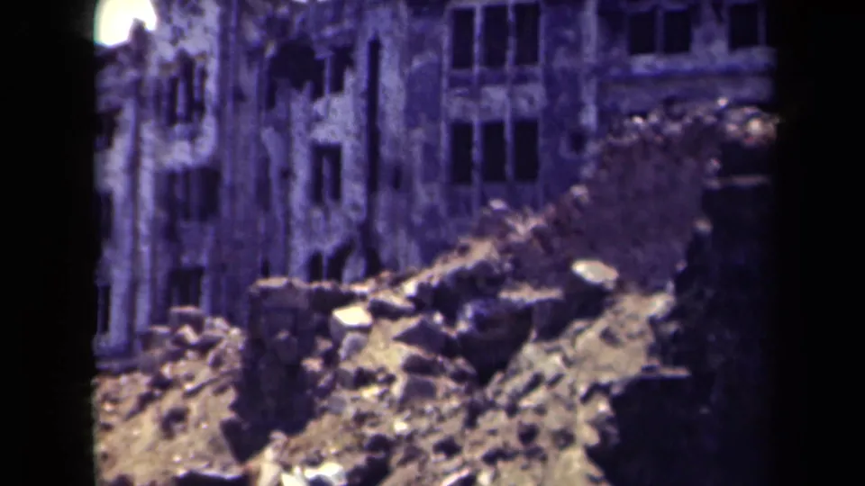 1944 Manila 8mm frame showing a damaged multi-story facade, rubble piles, and aged color shift from the film scan.