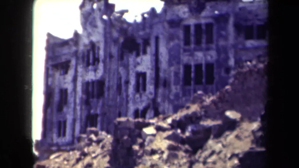 1944 Manila 8mm frame showing a ruined building face, rubble in the foreground, and a bright exposed strip at the film edge.