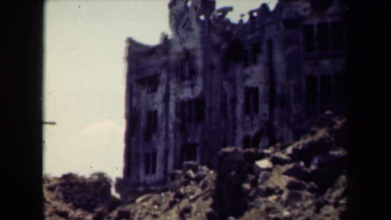 Ruined building corner with rubble and pale sky.