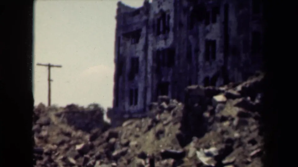 1944 Manila home-movie frame showing a ruined facade, debris in the foreground, and a utility pole near the left edge.
