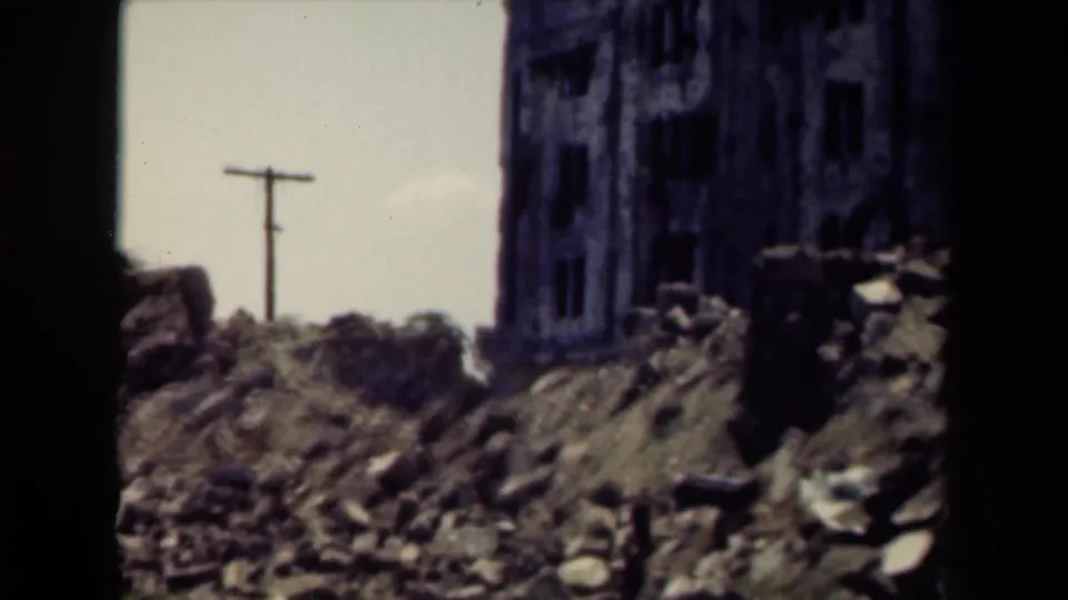 1944 Manila frame showing a rubble-strewn foreground, a utility pole, and the damaged edge of a large building at right.