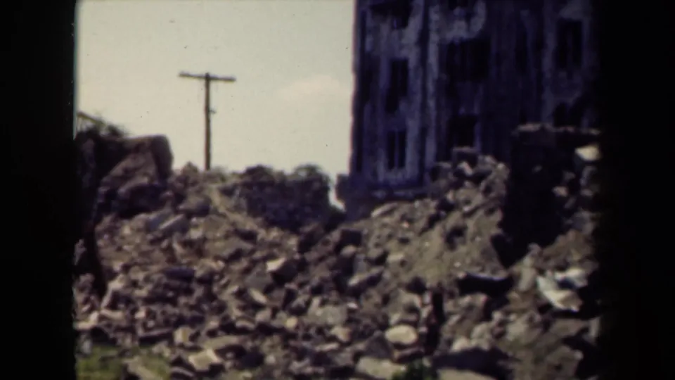 1940s Manila footage frame showing collapsed masonry, ruined wall sections, and a utility pole in a damaged Chinatown area.