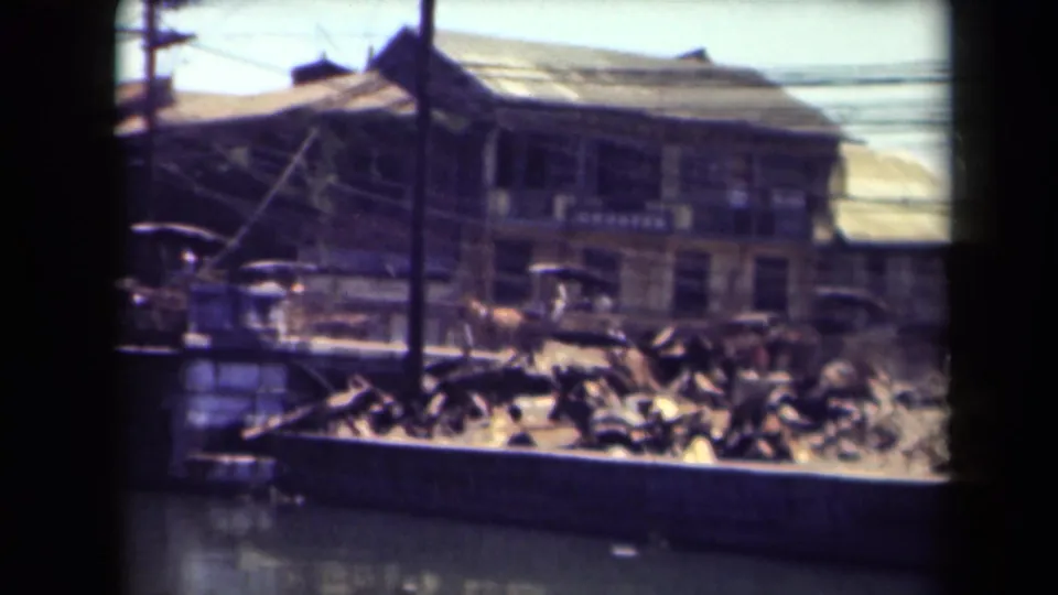 A Manila street scene across a waterfront, showing older buildings, a utility pole, wires, and debris or timber near the waterline.