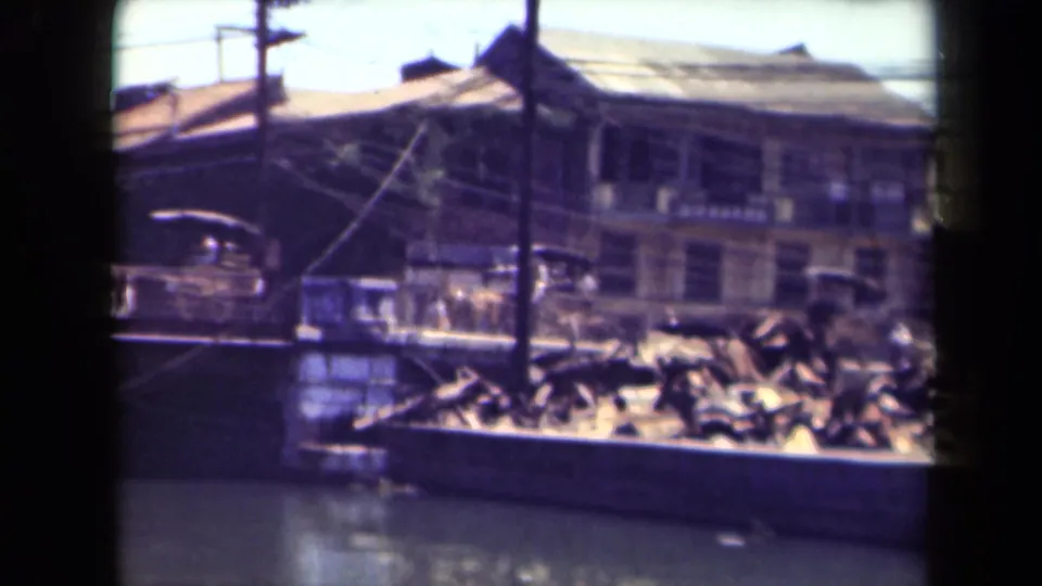 Soft 8mm view of a Manila waterfront street with older buildings, overhead wires, debris, and a possible horse-drawn carriage form in motion.