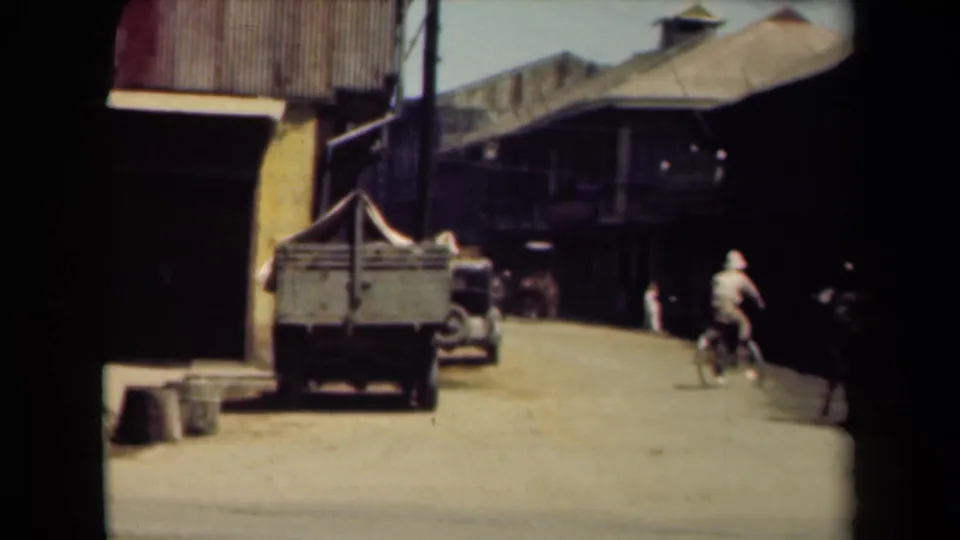 A Manila street view shows a bicyclist, pedestrians, a cart, and a parked vehicle beside low buildings in soft 8mm color.