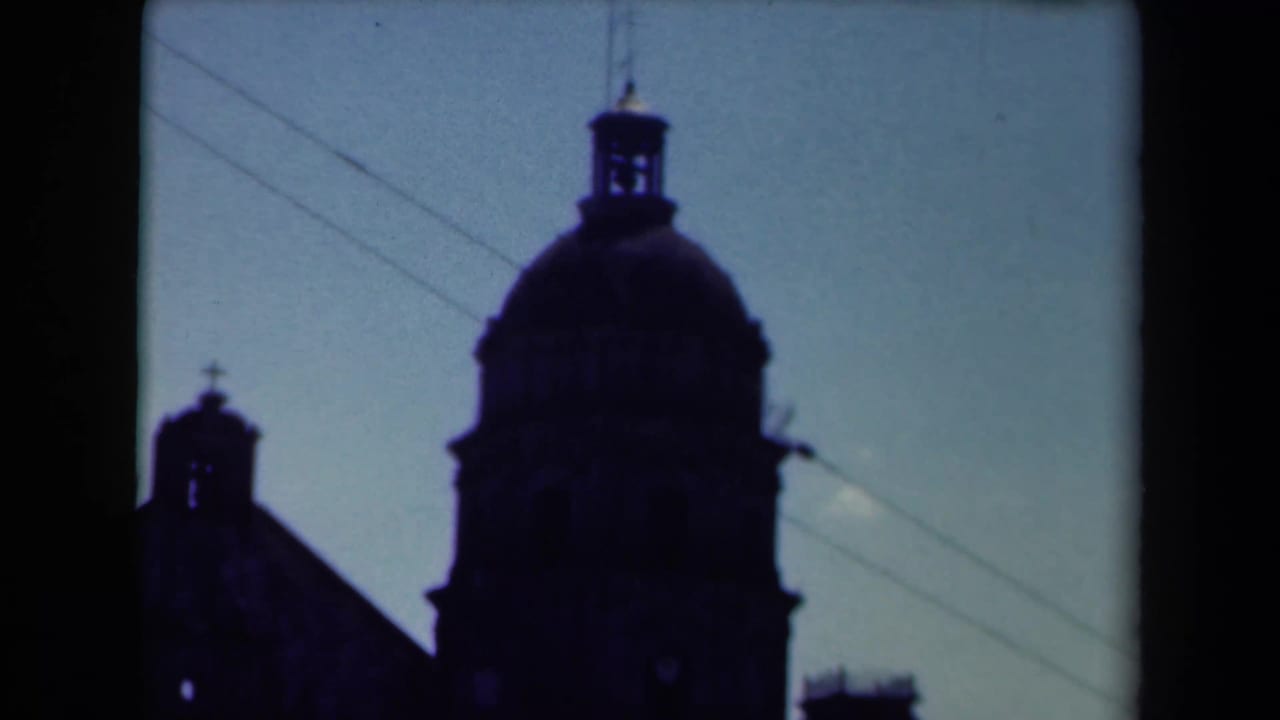 Dark cathedral dome and smaller bell tower silhouetted against a pale sky.