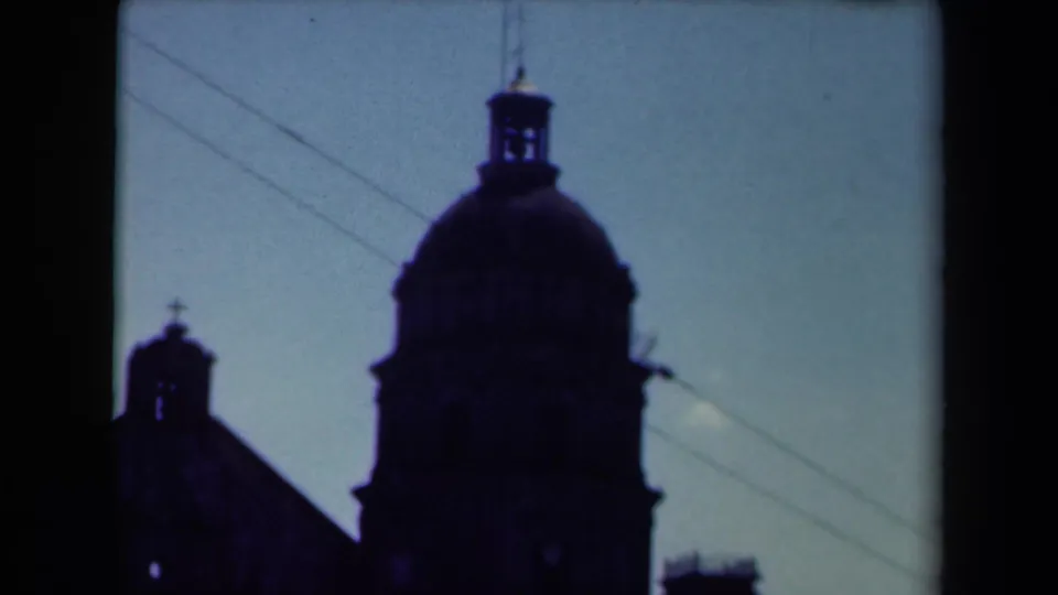1940s Manila footage showing a cathedral dome and smaller bell tower in silhouette, with utility wires crossing the sky.