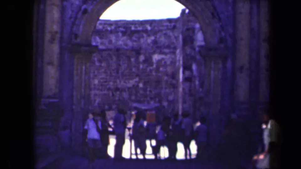 A small group of visitors stands within Manila church ruins, framed by a tall stone arch and weathered interior walls.