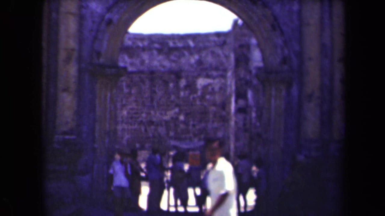 Visitors walk near a large weathered stone archway with a rough masonry wall beyond.