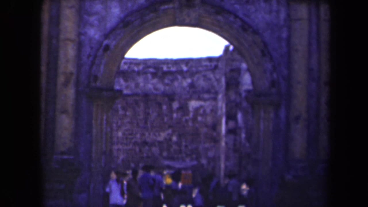 Visitors gather under a large stone archway at a Manila ruin site, captured in soft, blue-shifted 8mm footage.
