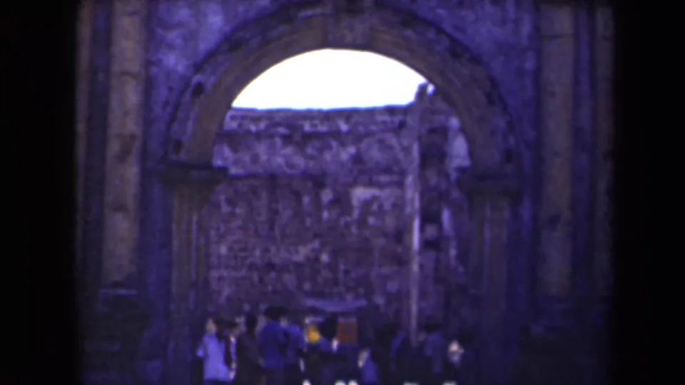Visitors gather under a large stone archway at a Manila ruin site, captured in soft, blue-shifted 8mm footage.