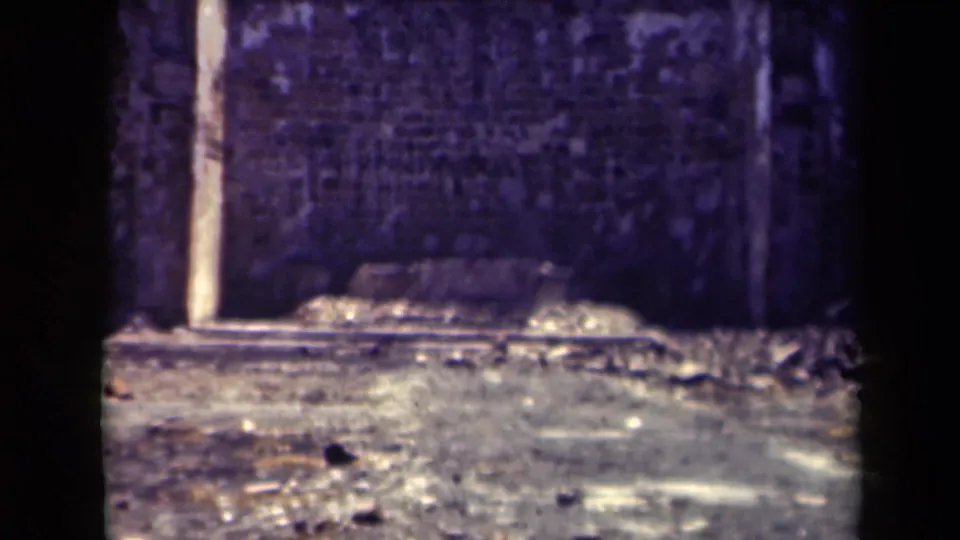 Final 8mm frame of a rough stone wall and open courtyard area at the Manila ruin site, with no clear figures centered.
