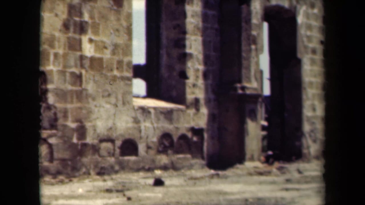 Sunlit stone building facade beside a street, with dark film edges and a partial view through the camera frame.