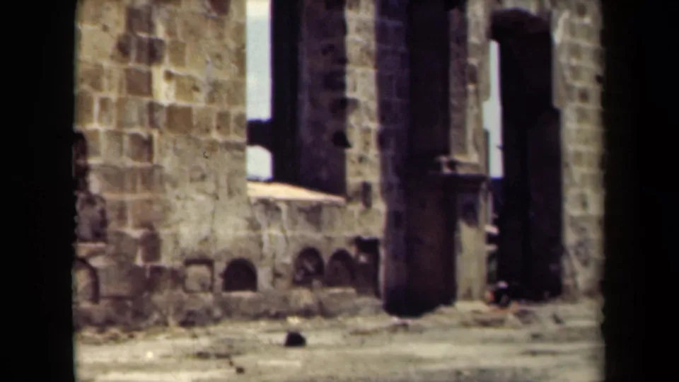 1940s Manila home-movie frame showing a sunlit stone or stucco building edge and street foreground, partly obscured by dark gate edges.