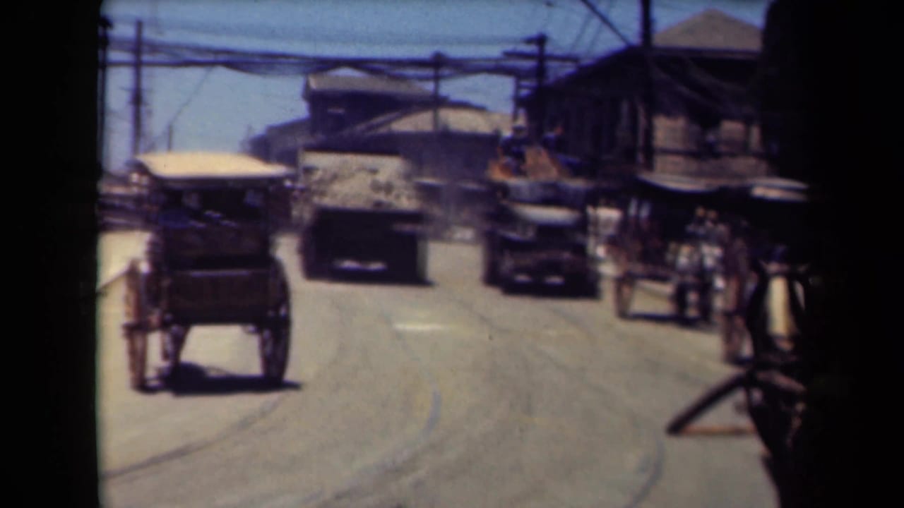 Horse-drawn buggy and motor vehicles travel along a bright city street with overhead wires.