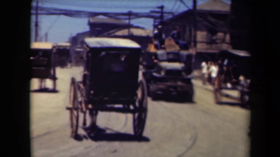 Rear view of a horse-drawn buggy in 1940s Manila traffic, with a dark automobile, roadside pedestrians, overhead wires, and simple buildings.