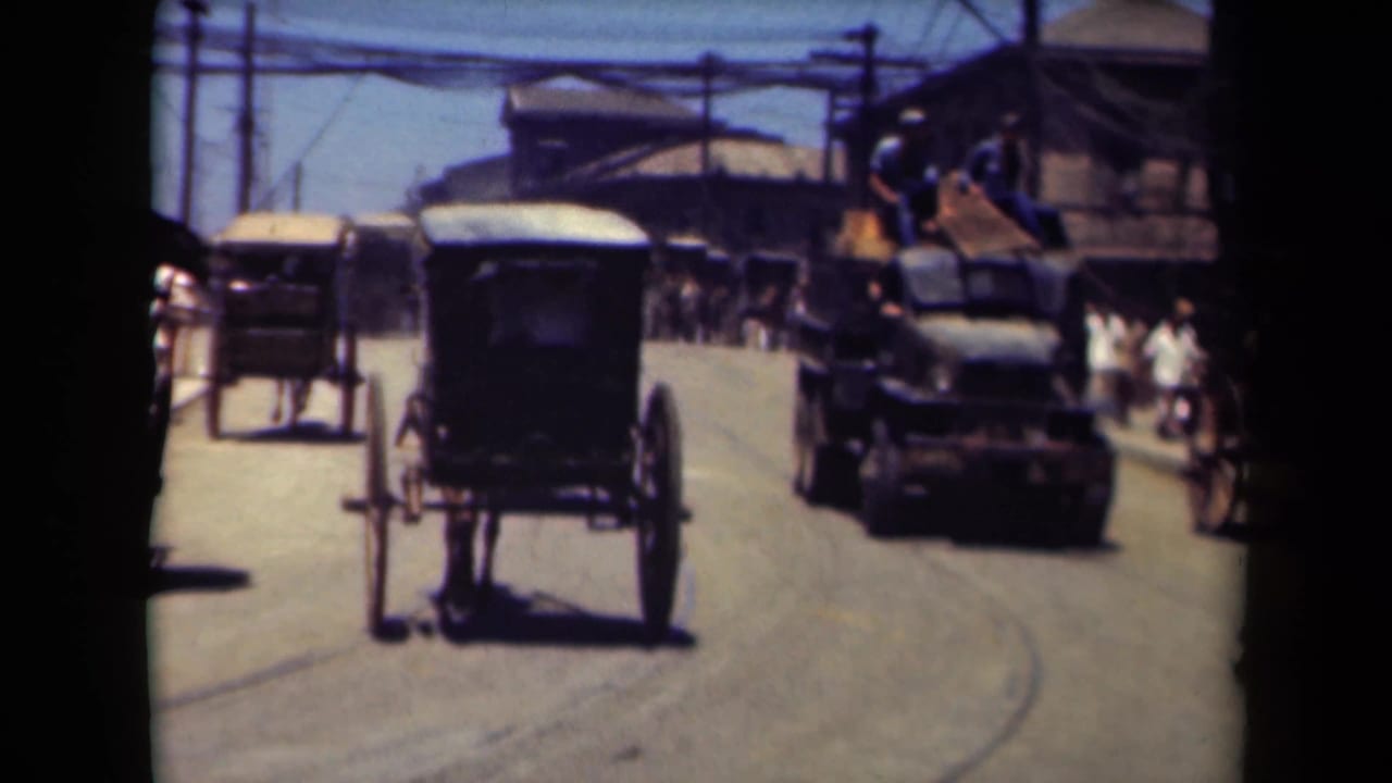 1944 Manila street view with carriages, an early motor vehicle, pedestrians and utility wires along a sunlit road.