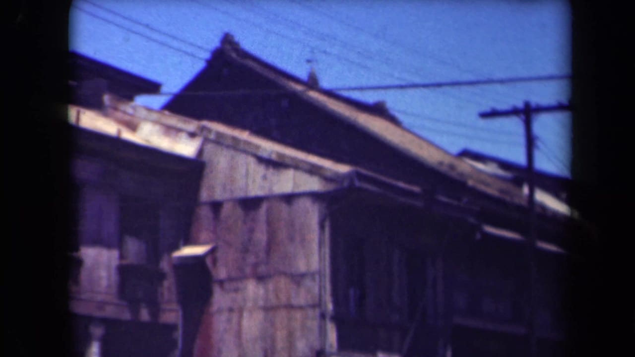 1940s 8mm frame, cataloged as Manila, showing a weathered wooden building with a tiled roof, utility pole, and overhead wires.