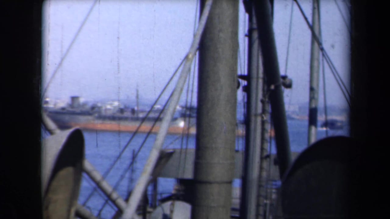 Ship rigging frames distant vessels on blue harbor water.