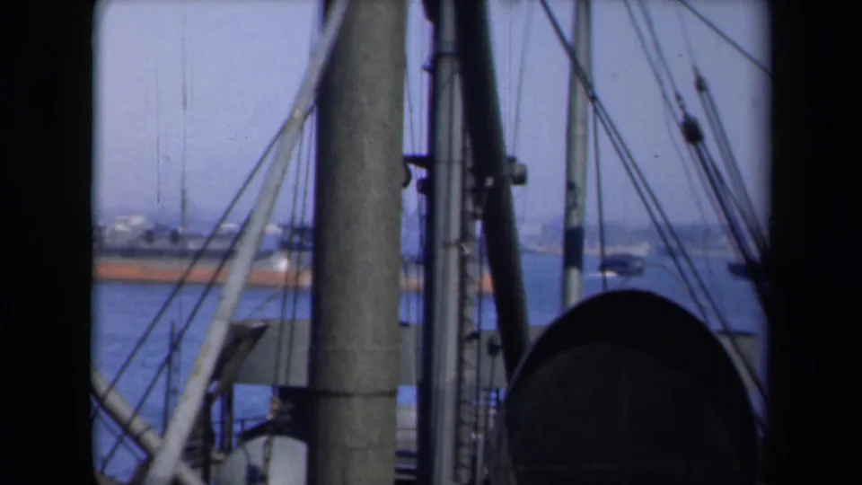 Shipboard 8mm view of New York harbor with rigging in front and ferry-like vessels in the distance.