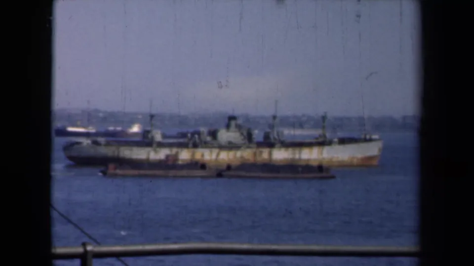 The final 1946 New York harbor frame holds on the cargo ship, tugboat activity, hazy skyline, railing, and 8mm film scratches.