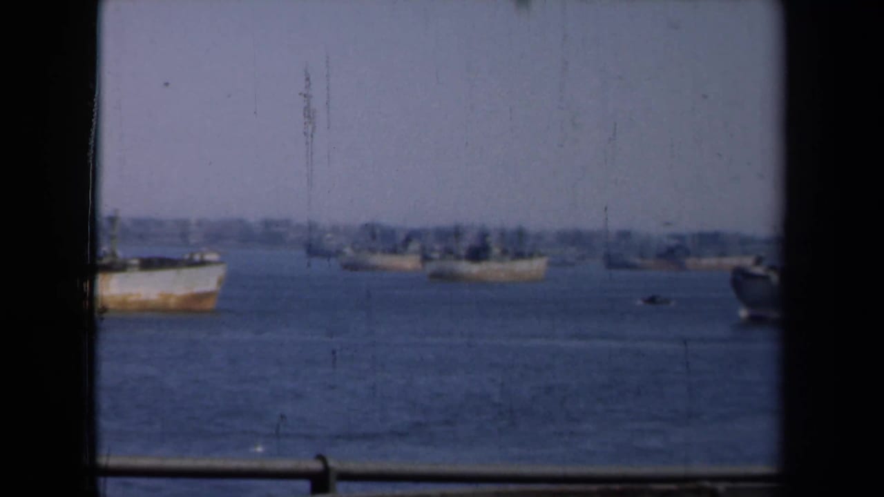 1946 New York harbor view with distant vessels on calm water, framed by dark window edges and hazy sky.