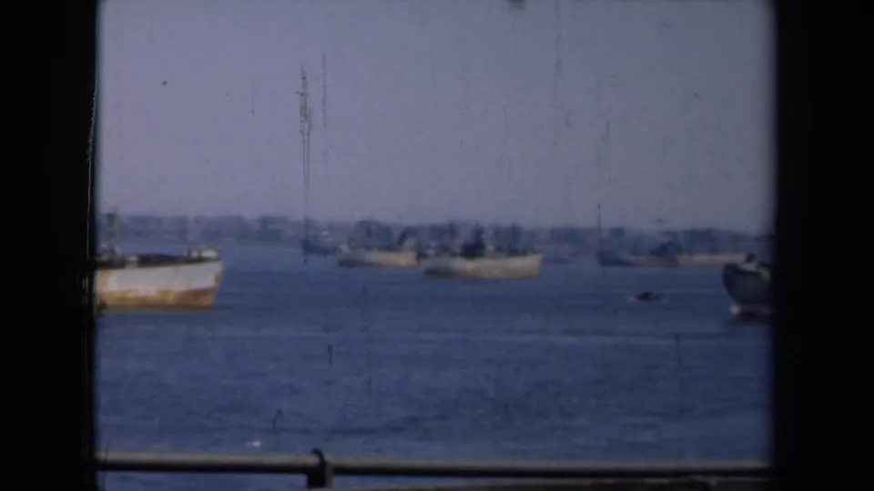 1946 New York harbor view with distant vessels on calm water, framed by dark window edges and hazy sky.