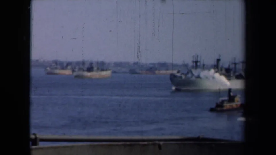A larger vessel moves across New York harbor in 1946, with smaller ships in the distance and a dark window edge in front.