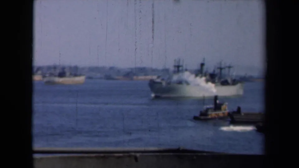 A steam-emitting ship crosses New York harbor in 1946 as a small tugboat moves near the dock in the foreground.