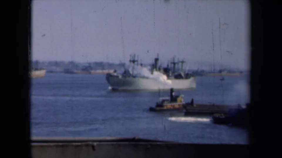 A steamship and tugboat share the New York harbor view in 1946, with a pier edge and distant shoreline visible through the frame.