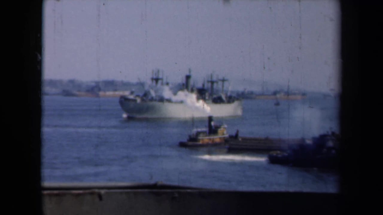1946 New York harbor view with a large gray ship in the distance and a tugboat crossing the foreground.