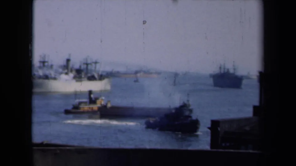 New York harbor scene with a foreground tugboat, part of a large ship at left, and a darker vessel in the distance.