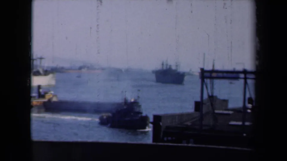 1946 New York harbor view through a dark window frame, with a small tugboat crossing near a pier and a larger ship offshore.
