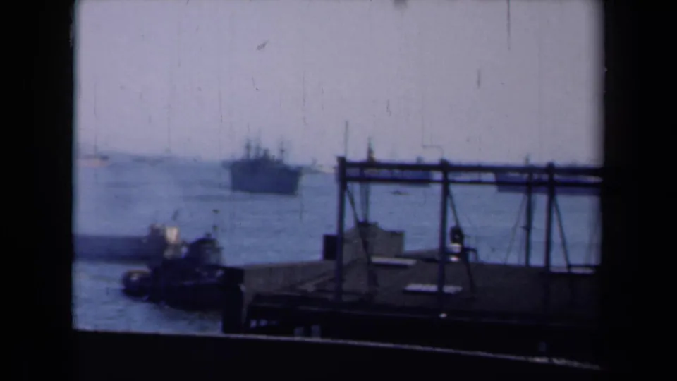 A 1946 New York harbor view from behind a window or dockside opening, showing a tugboat below and a larger vessel offshore.