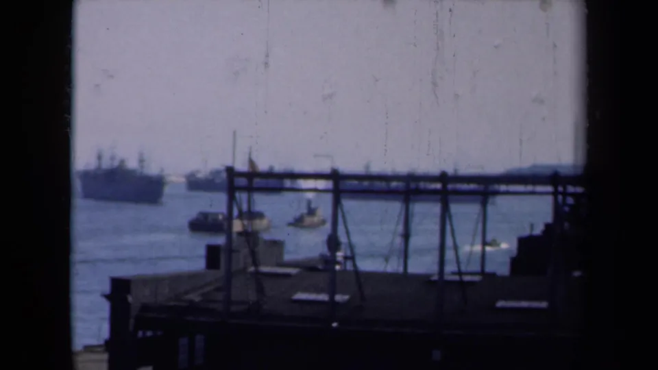 New York harbor in 1946, showing small boats, distant large ships, dock framework, and soft 8mm color.