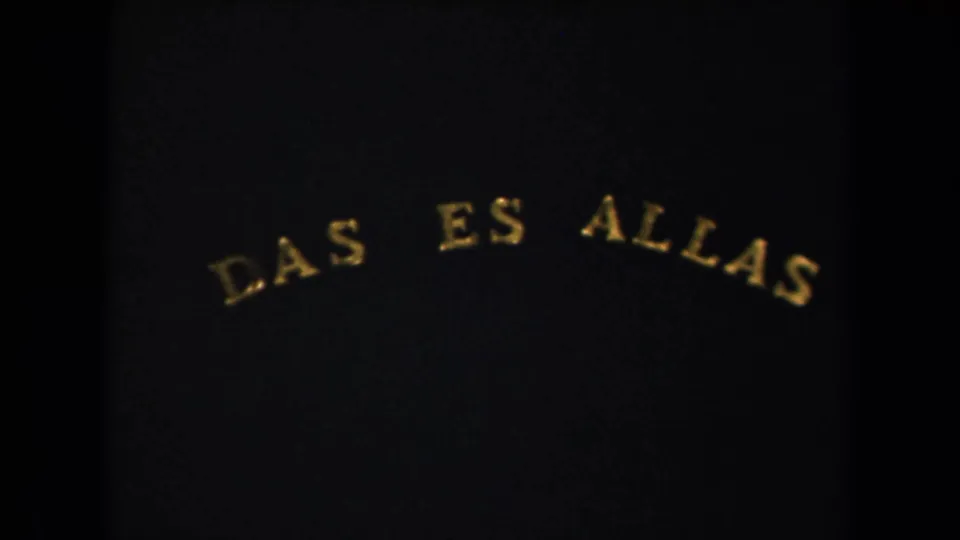 1940s 8mm frame from a New York-labeled reel showing a dark title card with arched gold lettering reading "DAS ES ALLAS."