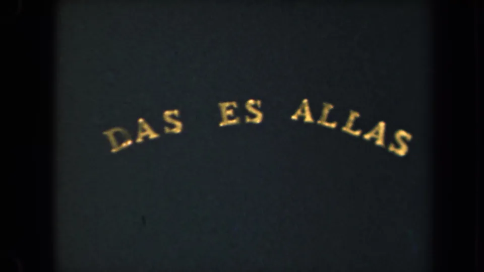 8mm frame showing the arched gold "DAS ES ALLAS" title lower in the composition, with visible grain and dark gate edges.