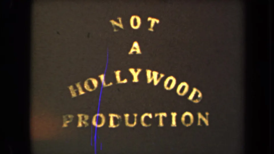 1946 8mm frame showing the NOT A HOLLYWOOD PRODUCTION card with visible grain and a blue scratch line.