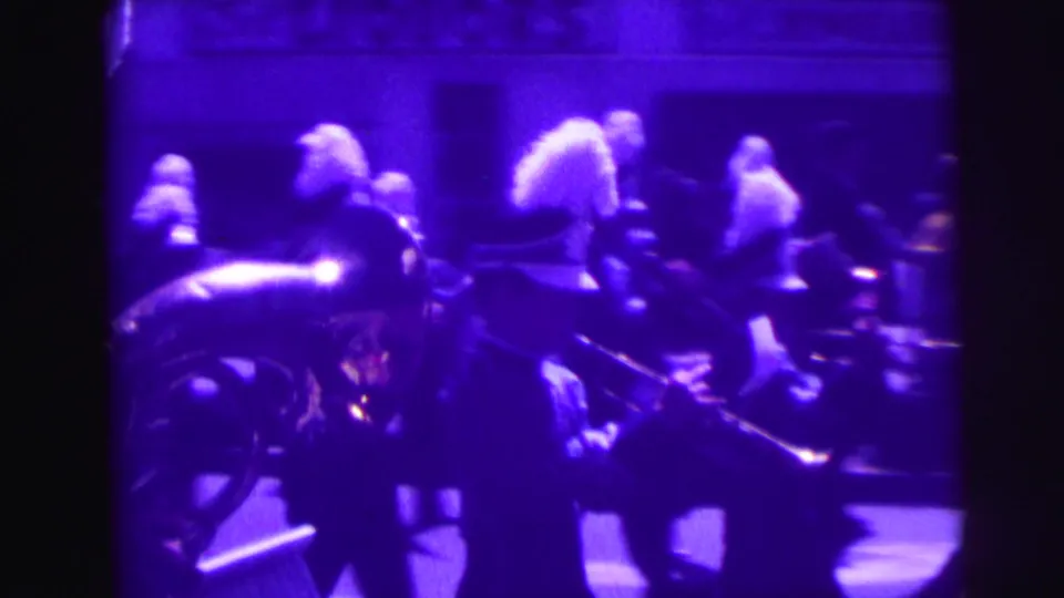Uniformed marching band performers with feathered hats and brass instruments pass through a purple-shifted street scene.